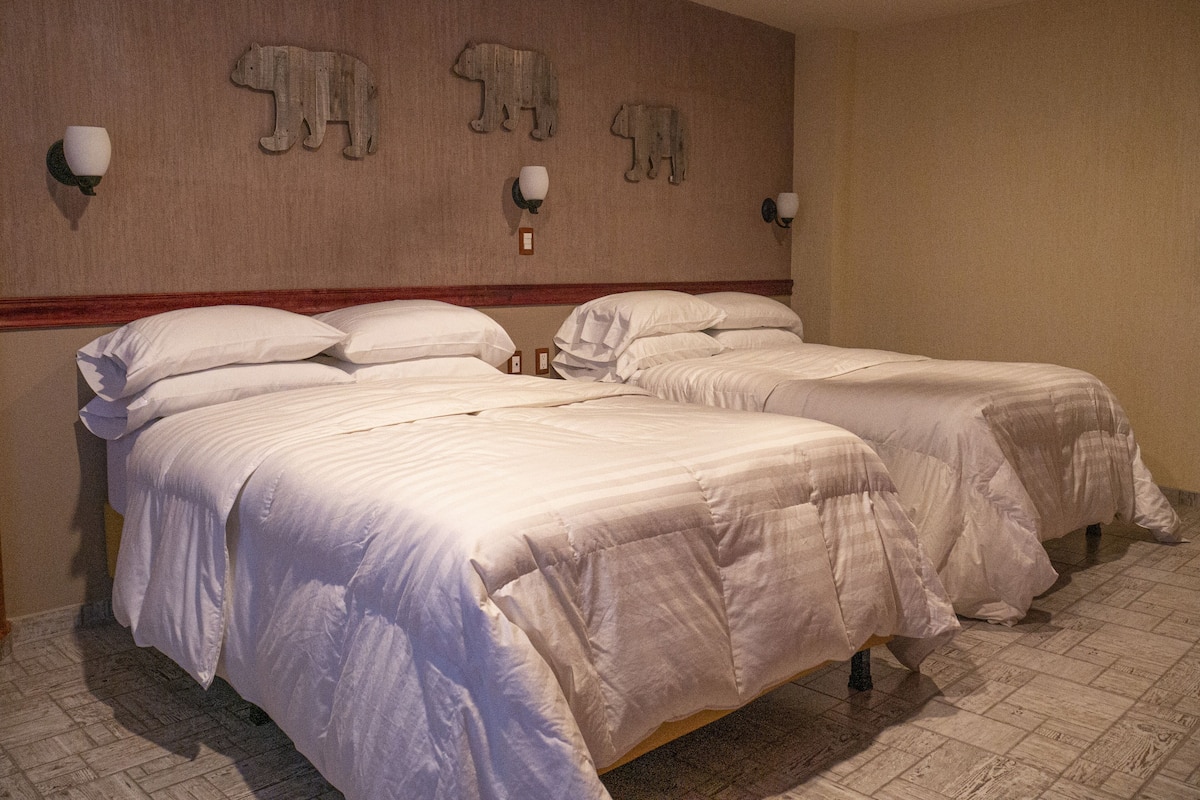Une chambre d’hôtel avec deux lits, une tête de lit en bois, des appliques murales et un ventilateur de plafond.