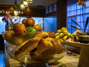 A table with a fruit bowl containing oranges, a watermelon, and bananas. There are also baguettes and a small bowl with a plant. - Hotel el Cóndor (Cortazar)