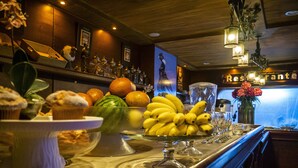 A bar area with a fruit display including bananas, oranges, and a watermelon, along with various glasses and a vase of flowers. - Hotel el Cóndor (Cortazar)