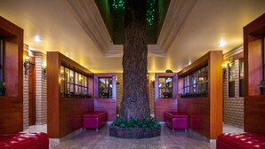 A lobby with a large tree, red seating, and brick walls. - Hotel el Cóndor (Cortazar)