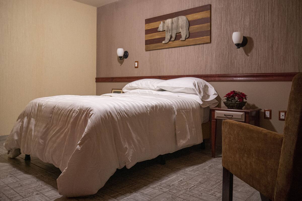 Une chambre d’hôtel avec un grand lit, une table de chevet avec une lampe, une chaise et une œuvre d’art représentant un ours, accrochée au mur.
