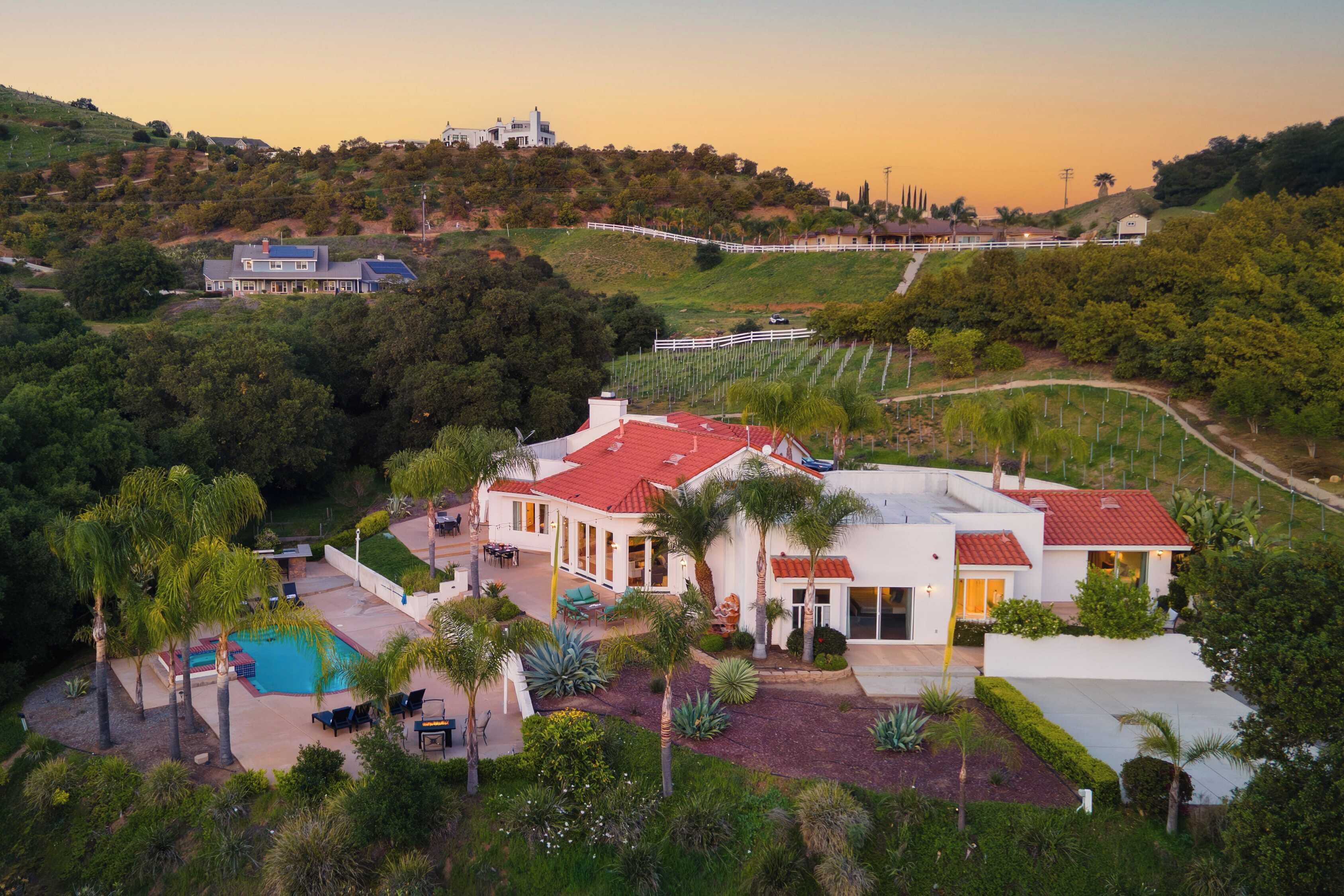 Ein großes Haus mit Swimmingpool, umgeben von üppiger Vegetation und einer hügeligen Landschaft.