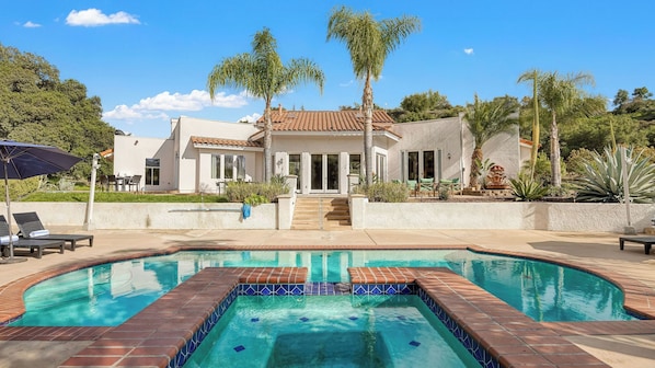 Une piscine bordée de carreaux, une maison avec un toit en tuiles et des palmiers.