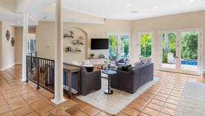 A spacious living area with a fireplace, comfortable seating, and a large window overlooking a garden. - Grapevine by Avantstay Secluded 5BR Villa 4 Acres of Vineyards & Avo Groves! (Temecula)