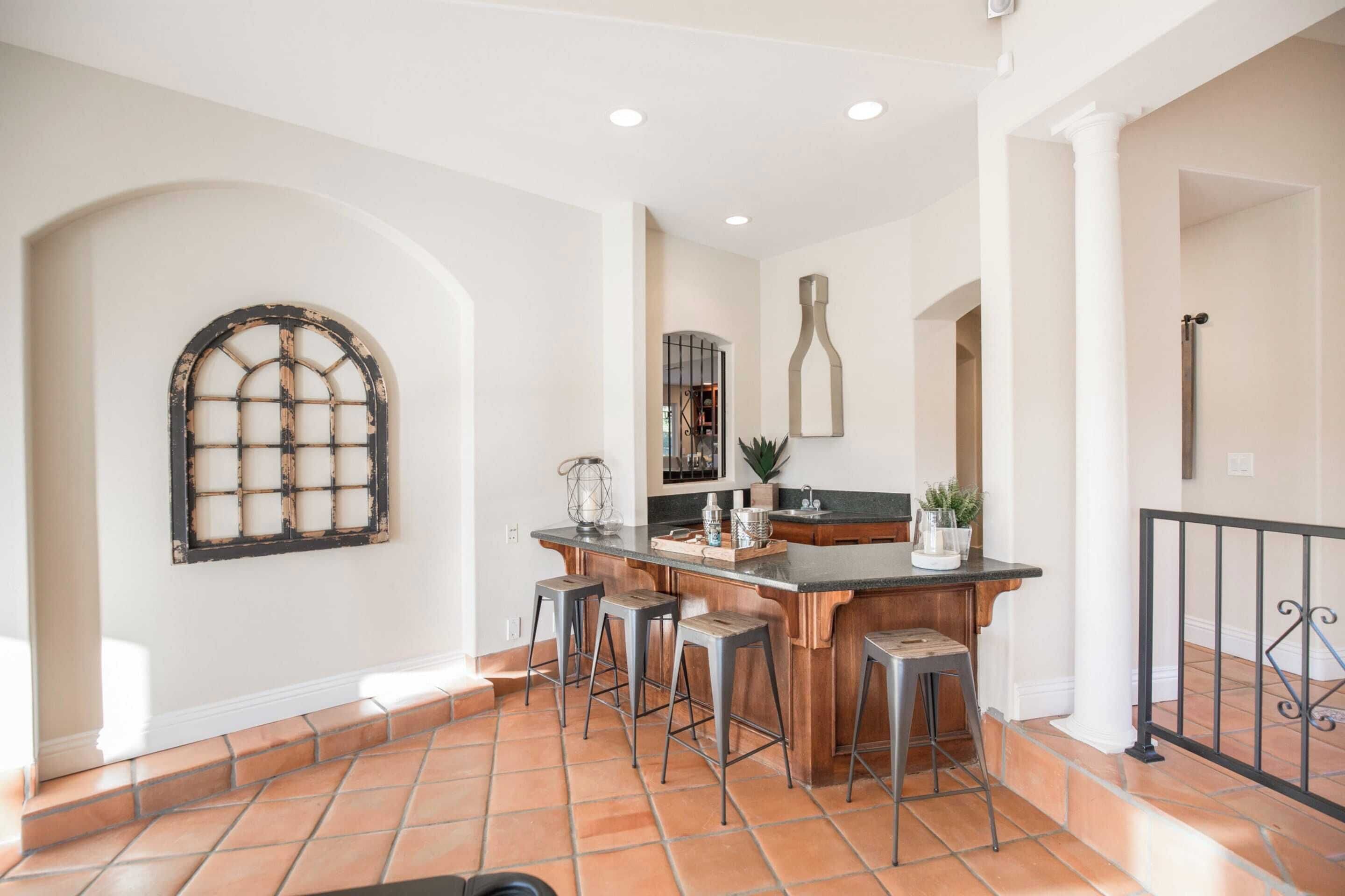 A kitchen with a bar area, stools, and a large window with a grid design.