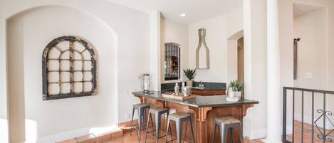 A kitchen with a bar area, stools, and a large window with a grid design.