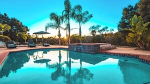 A swimming pool with tiled edges, lounge chairs, and umbrellas. - Grapevine by Avantstay Secluded 5BR Villa 4 Acres of Vineyards & Avo Groves! (Temecula)