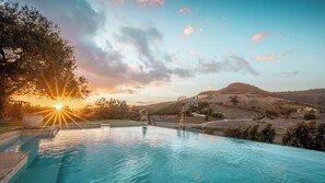 A swimming pool with a sunset in the background, a windmill, and a hilly landscape.