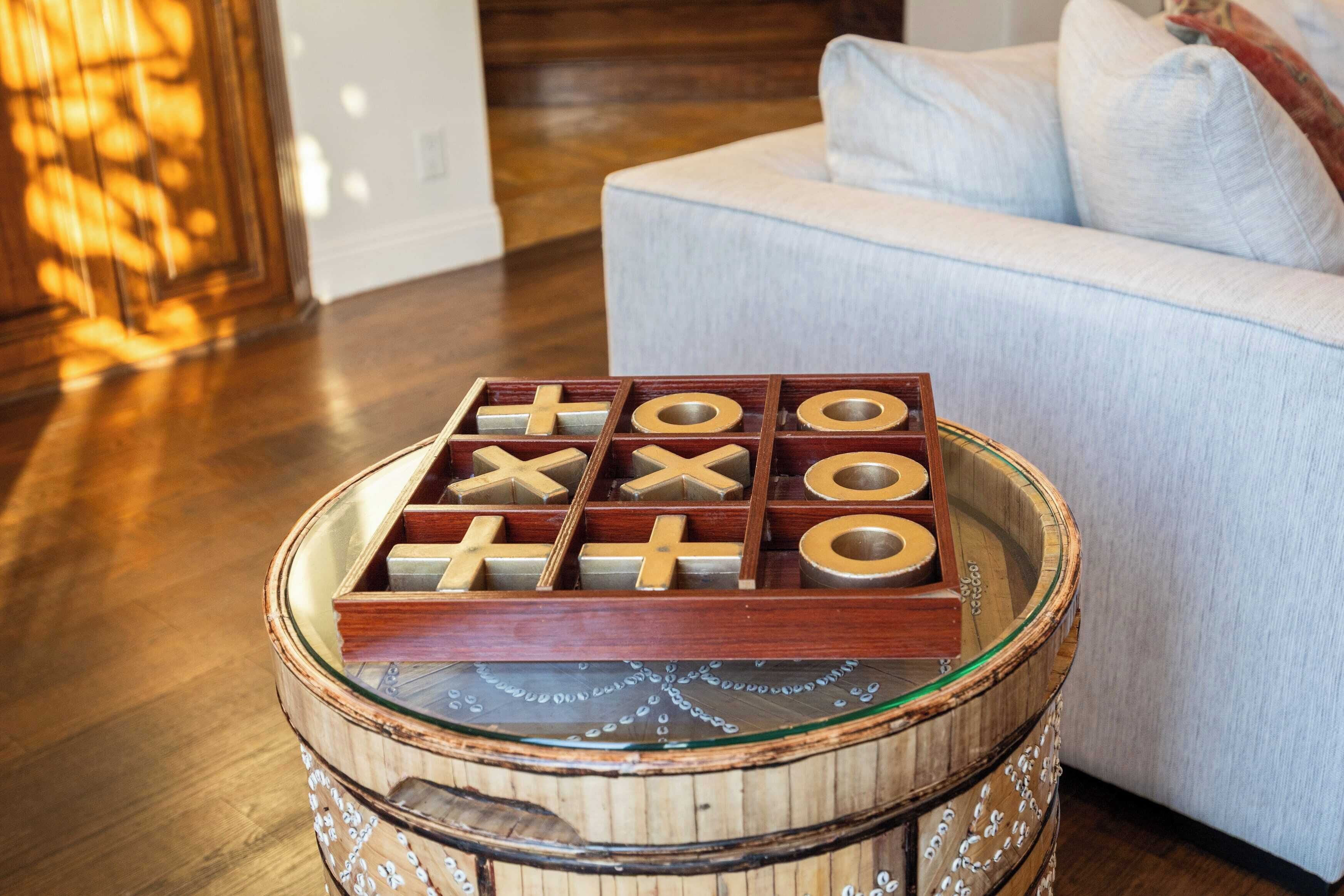 A tic-tac-toe game on a wooden table with a glass top, placed in a room with a light blue sofa and wooden flooring.