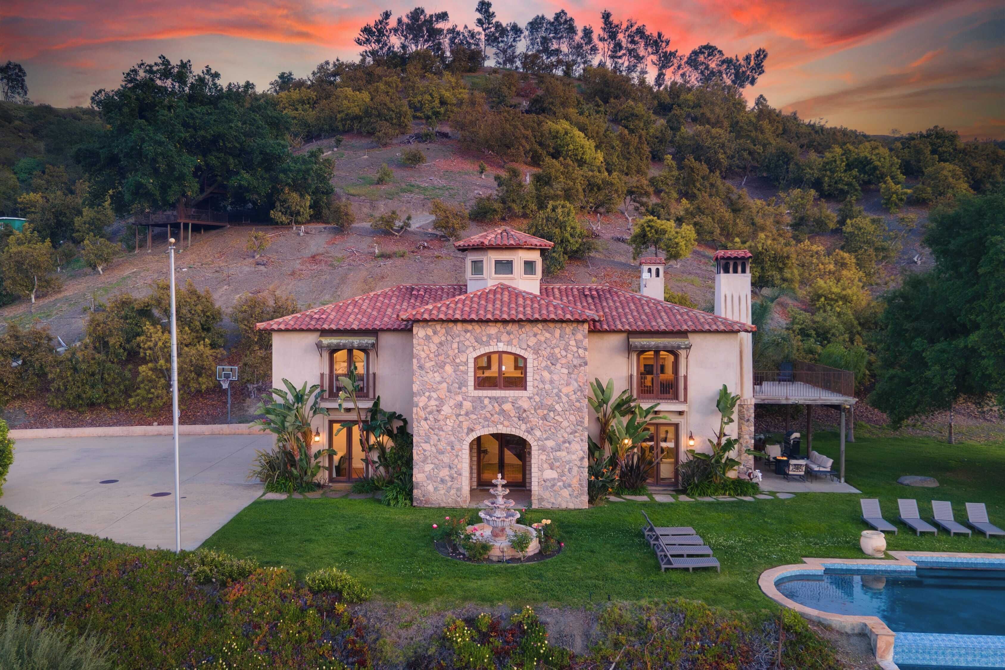 A two-story house with a stone facade, a swimming pool, and a well-maintained garden.