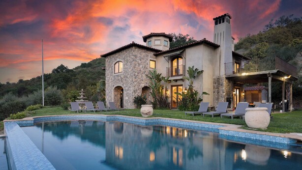 A luxurious house with a swimming pool, stone walls, and a balcony overlooking the pool.