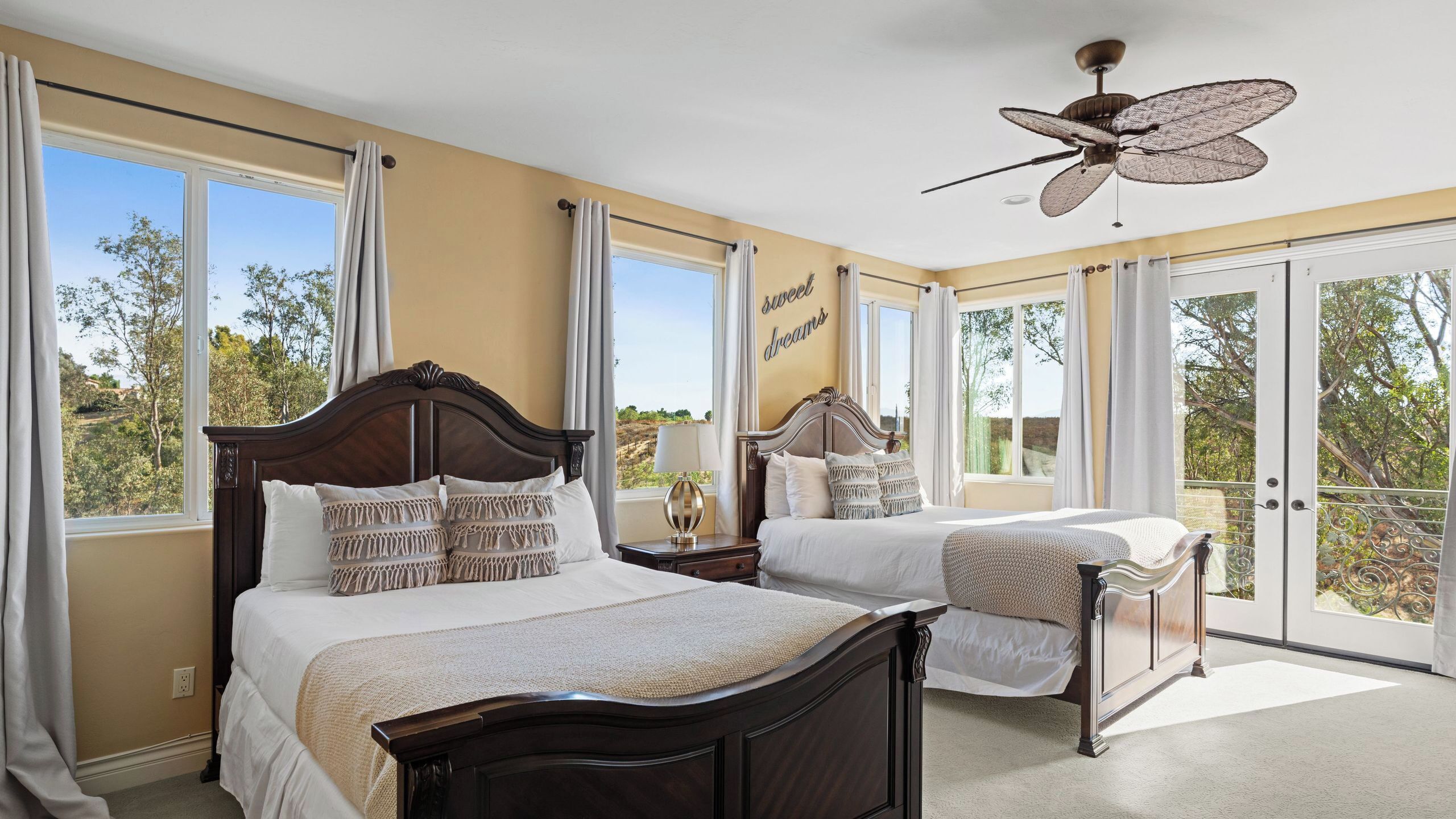 A bedroom with two beds, a ceiling fan, large windows, and a balcony.