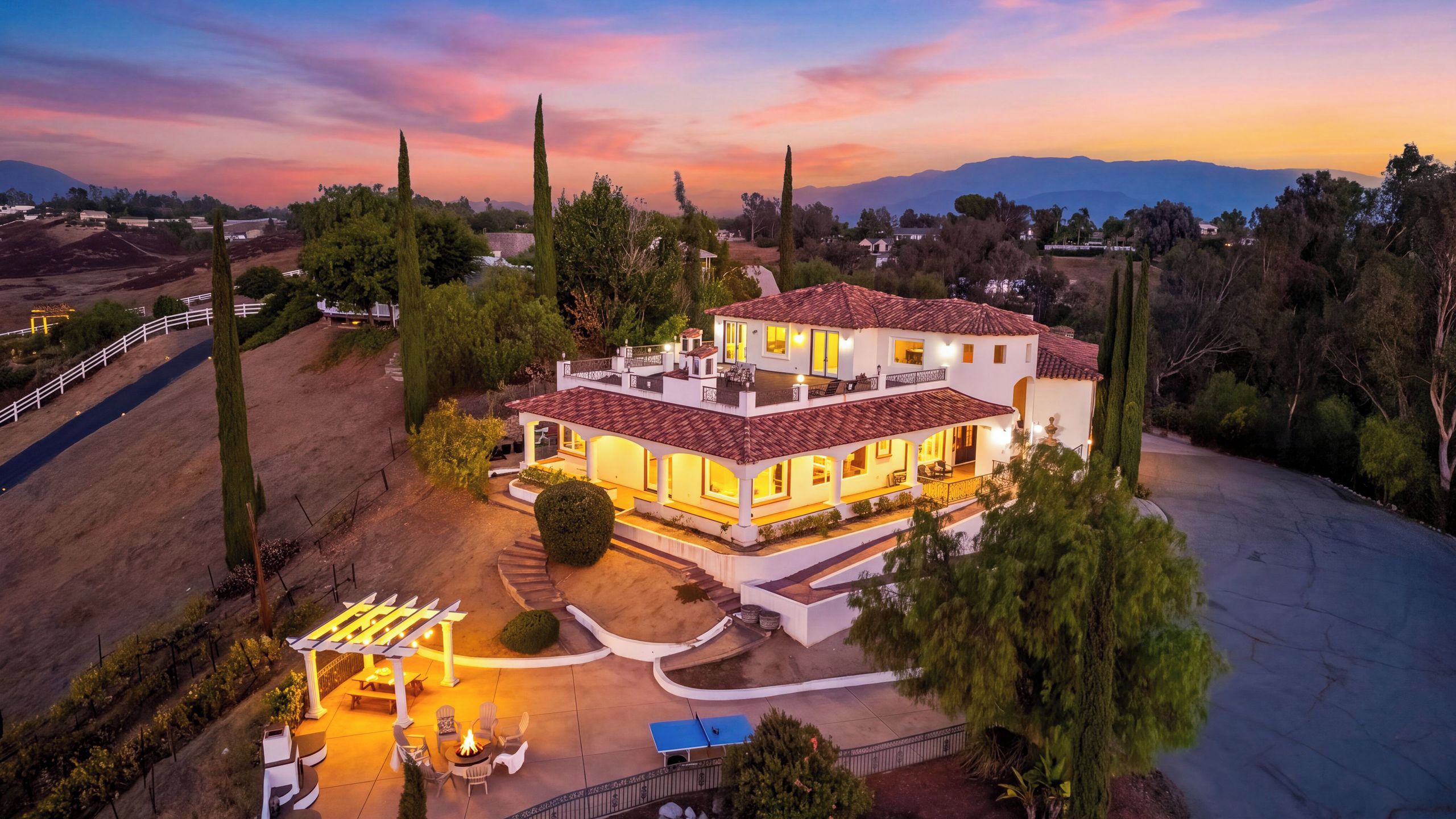 A two-story house with a patio, a fire pit, and a view of the surrounding landscape.