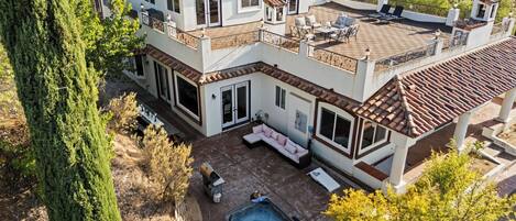 A multi-story house with a patio, outdoor seating, and a hot tub.