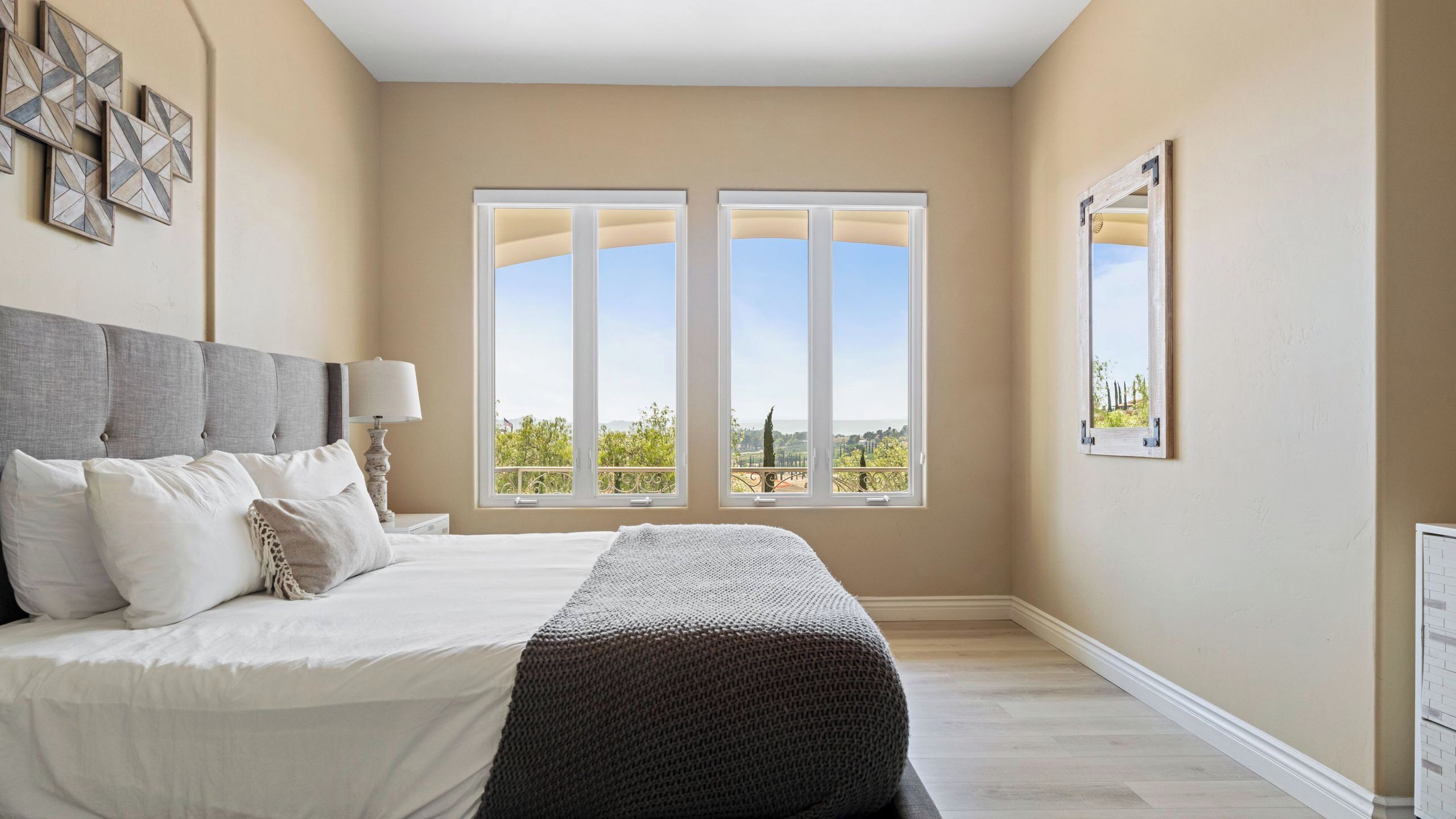 A bedroom with a large bed, two windows, a bedside table, and a lamp.