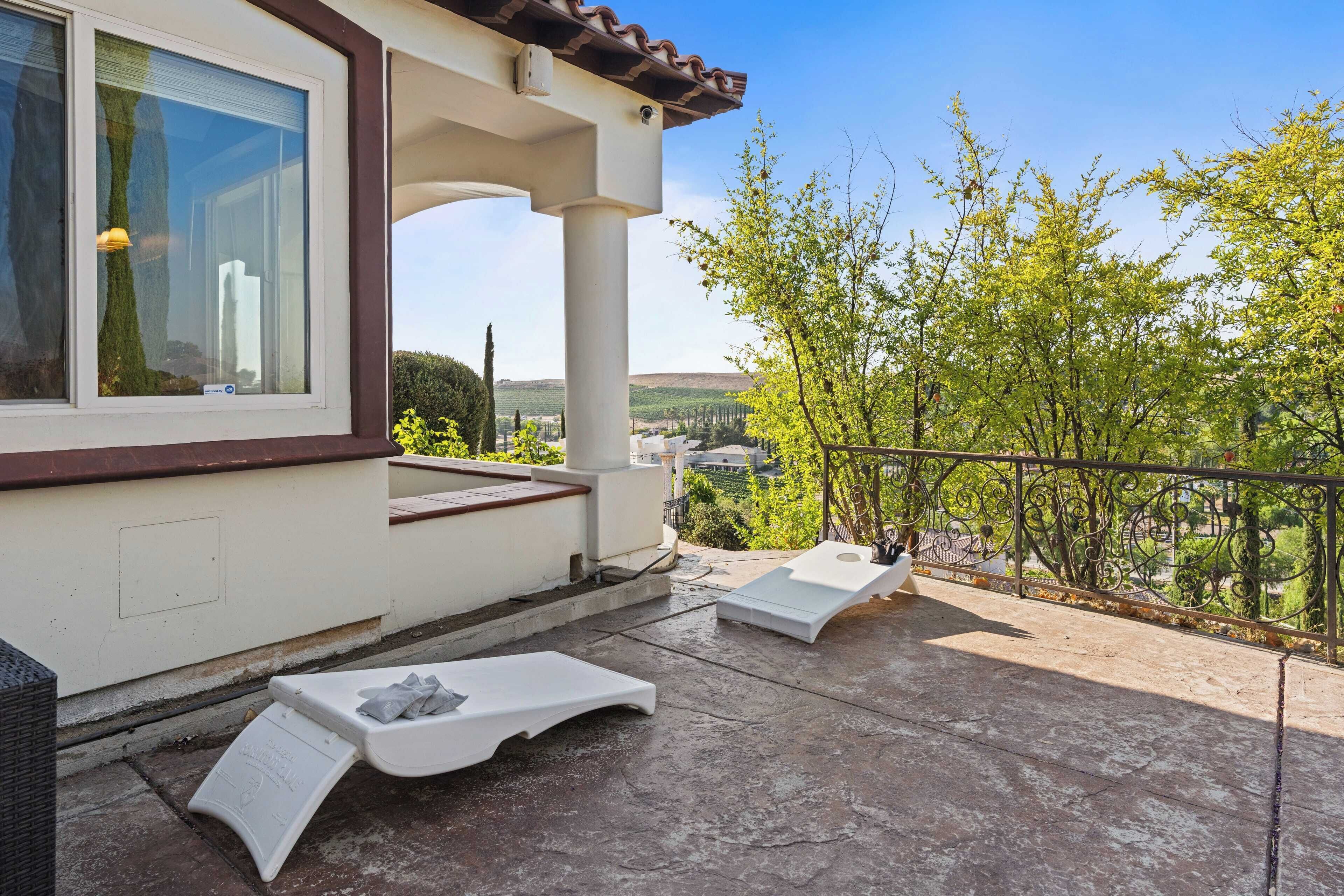 A balcony with two sun loungers and a small table, overlooking a green landscape with trees and buildings.