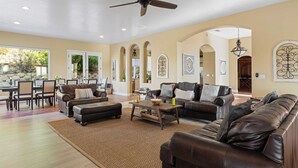 A spacious living room with a ceiling fan, leather sofas, a coffee table, and a dining area with chairs and a table. - Wine Country Villa Large Rooftop Terrace w/ Views + Game Room Via del Sur (Temecula)