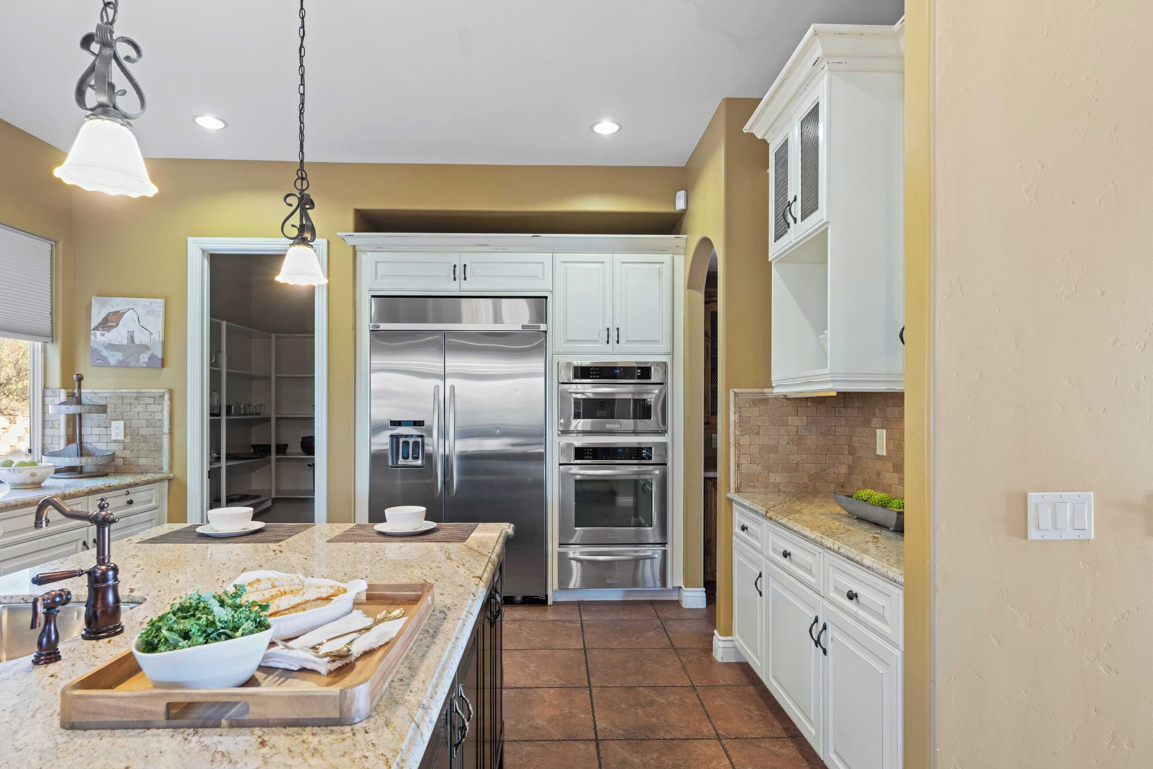 A modern kitchen with white cabinetry, stainless steel appliances, and a marble countertop.