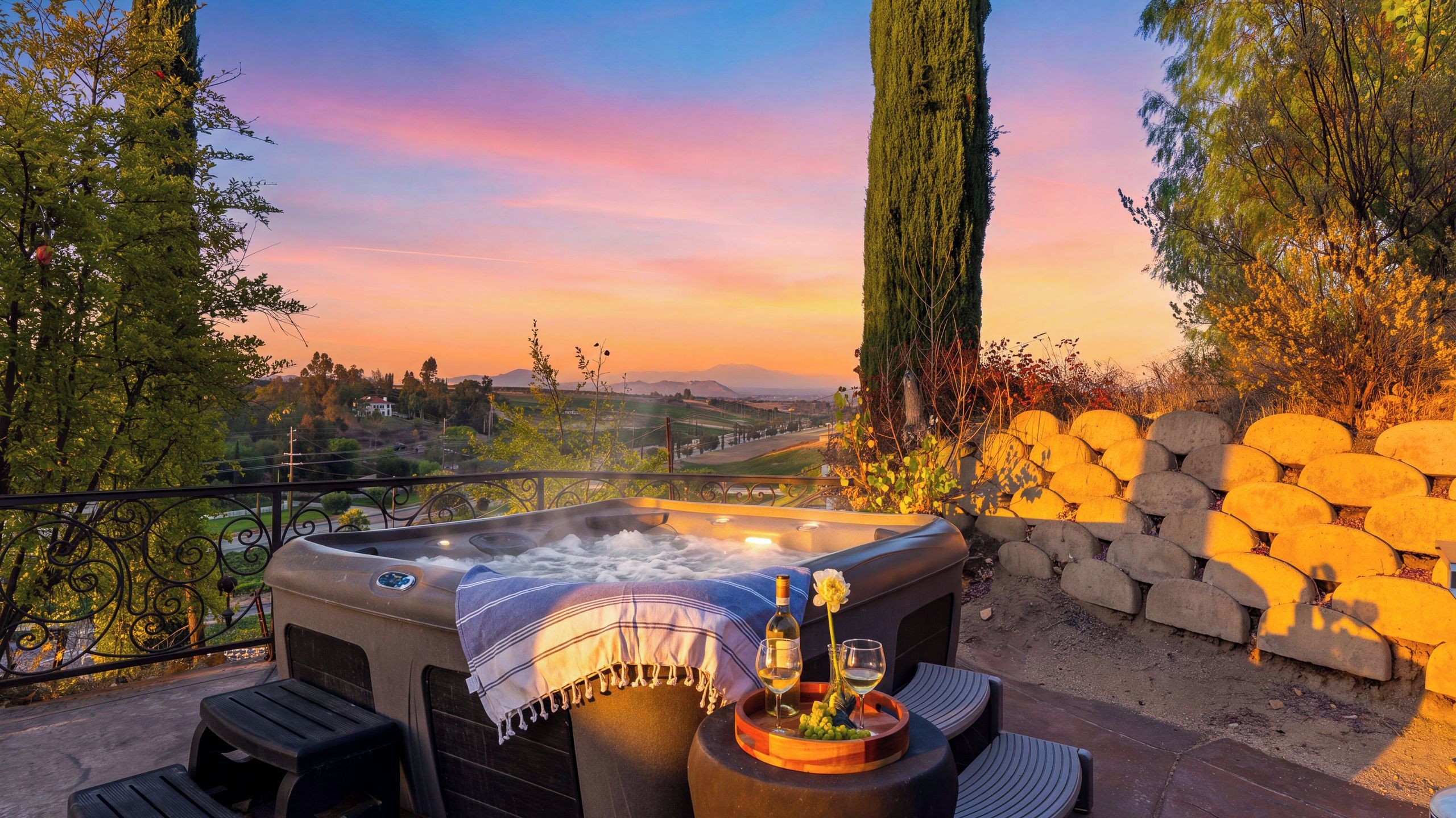 A hot tub with a view of a landscape, outdoor seating, and a stone wall.