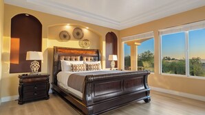 A bedroom with a large bed, two bedside tables, a view of the outdoors, and decorative wall art. - Wine Country Villa Large Rooftop Terrace w/ Views + Game Room Via del Sur (Temecula)