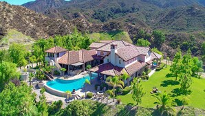 A large house with a swimming pool, surrounded by lush greenery and mountains in the background. - Owl's Nest by Avantstay Infinity Pool w/ Incredible Views (Temecula)