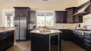 Una cocina moderna con armarios oscuros, un refrigerador de acero inoxidable, horno empotrado y una isla grande con encimera de granito.