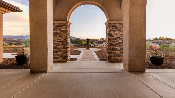 Un patio cubierto con pilares de piedra y vistas a un jardín ajardinado.