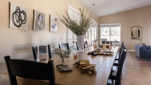 Un comedor con una mesa larga, sillas, un florero con plantas y obras de arte enmarcadas en la pared.