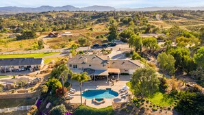 A large house with a swimming pool, surrounded by a well-maintained garden and a view of distant mountains. - Willow by Avantstay Mountain Views - See Hot Air Balloons From Pool (Temecula)