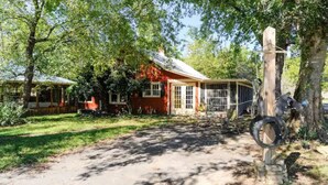A rustic house with a red exterior, a covered porch, and a wooden swing set.