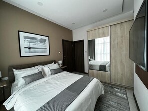 Une chambre d’hôtel moderne, dotée d’un grand lit, d’un téléviseur à écran plat, d’une armoire et d’un tableau encadré au mur.