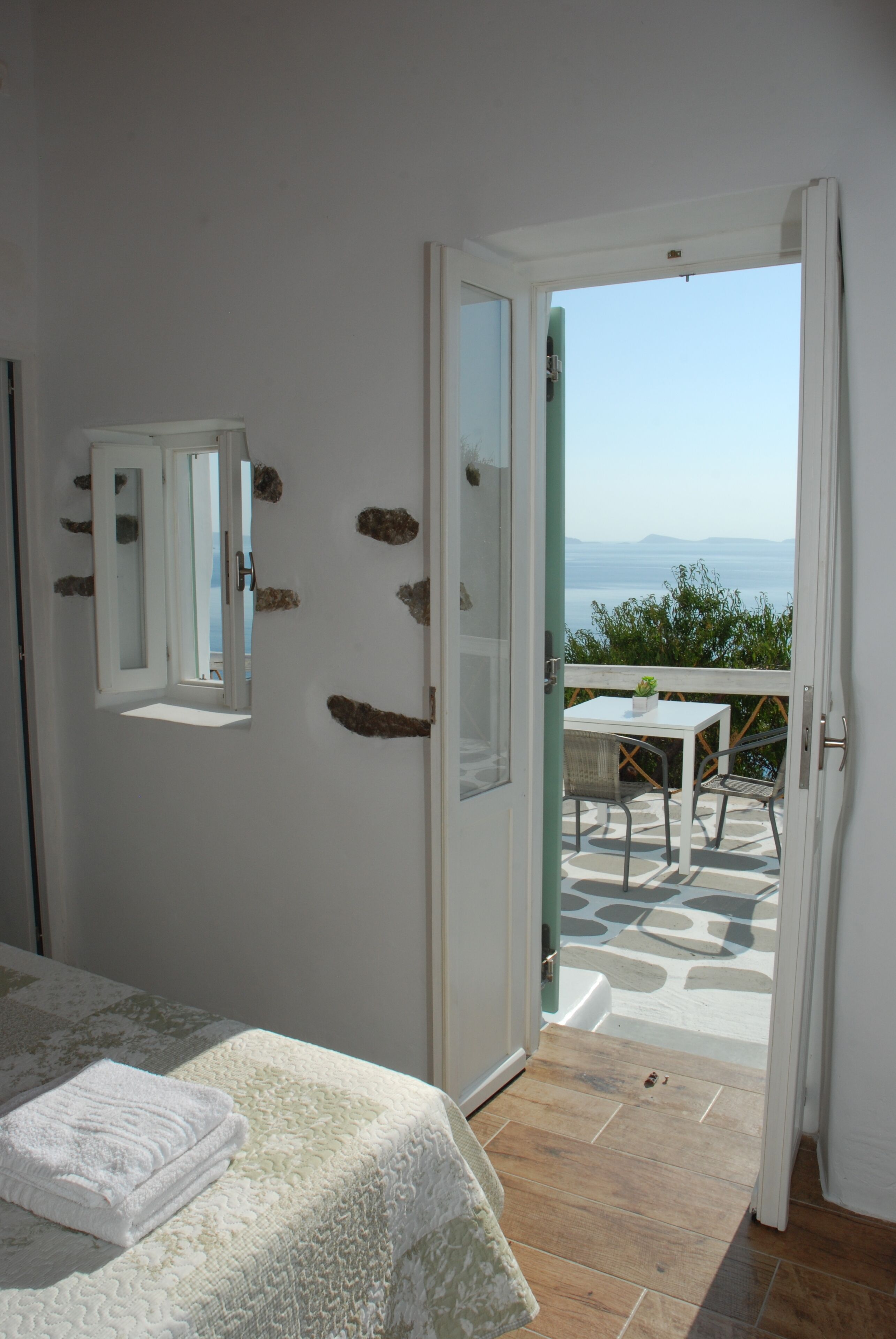 A bedroom with a bed, a bathroom mirror, and a balcony with a table and chairs.