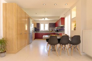 A modern kitchen with wooden cabinets, a dining area with a table and chairs, and a central island. - Blue Sky Villa in Crete (heraklion)