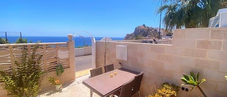 A patio with a table and chairs, a view of the sea, and some plants.