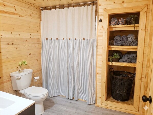 Une salle de bain en bois avec des toilettes, un rideau de douche à rayures et un meuble en bois contenant des serviettes et des plantes.
