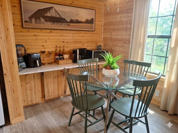 Un interior de madera con una mesa de comedor de vidrio, sillas, una estación de café y un ventanal grande.
