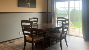 A dining room with a wooden table and chairs, a large window with a view of greenery, and a deer antler artwork on the wall.