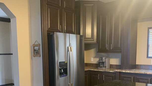 A kitchen with dark wood cabinets, a stainless steel refrigerator, granite countertops, and a built-in island with seating.