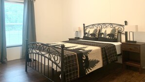 A bedroom with a metal bed frame, a plaid blanket, two bedside lamps, and a window with curtains.