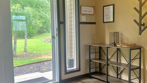 A room with a sliding glass door leading to a garden, a framed certificate on the wall, and a small table with a lamp.