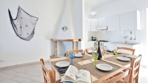 Un coin repas moderne avec une table en bois dressée pour quatre personnes, entourée de chaises. Un livre est ouvert sur la table, et on y trouve des verres à vin et une bougie posés sur la nappe.
