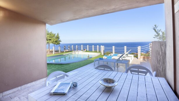 Un balcon avec une table en bois, des chaises et une vue sur la mer et une piscine.