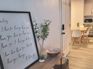 A framed love quote on a wall, a vase with a plant, and a dining area with a table and chairs.