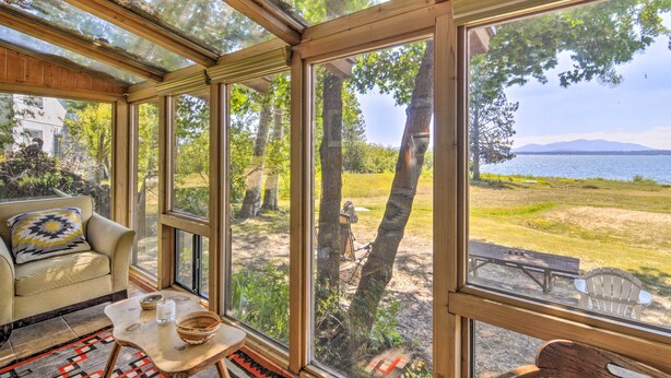 Una habitación luminosa con ventanas amplias, un sofá, una mesita y vistas a un lago y árboles.