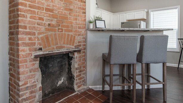 A kitchen with a brick fireplace, two barstools, and a countertop with cabinets. - The Pink Pearl / 5 Min to Rupp / Newly Remodeled (Lexington)