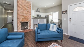 A modern living room with a blue sofa, a brick fireplace, and a kitchen in the background. - The Pink Pearl / 5 Min to Rupp / Newly Remodeled (Lexington)