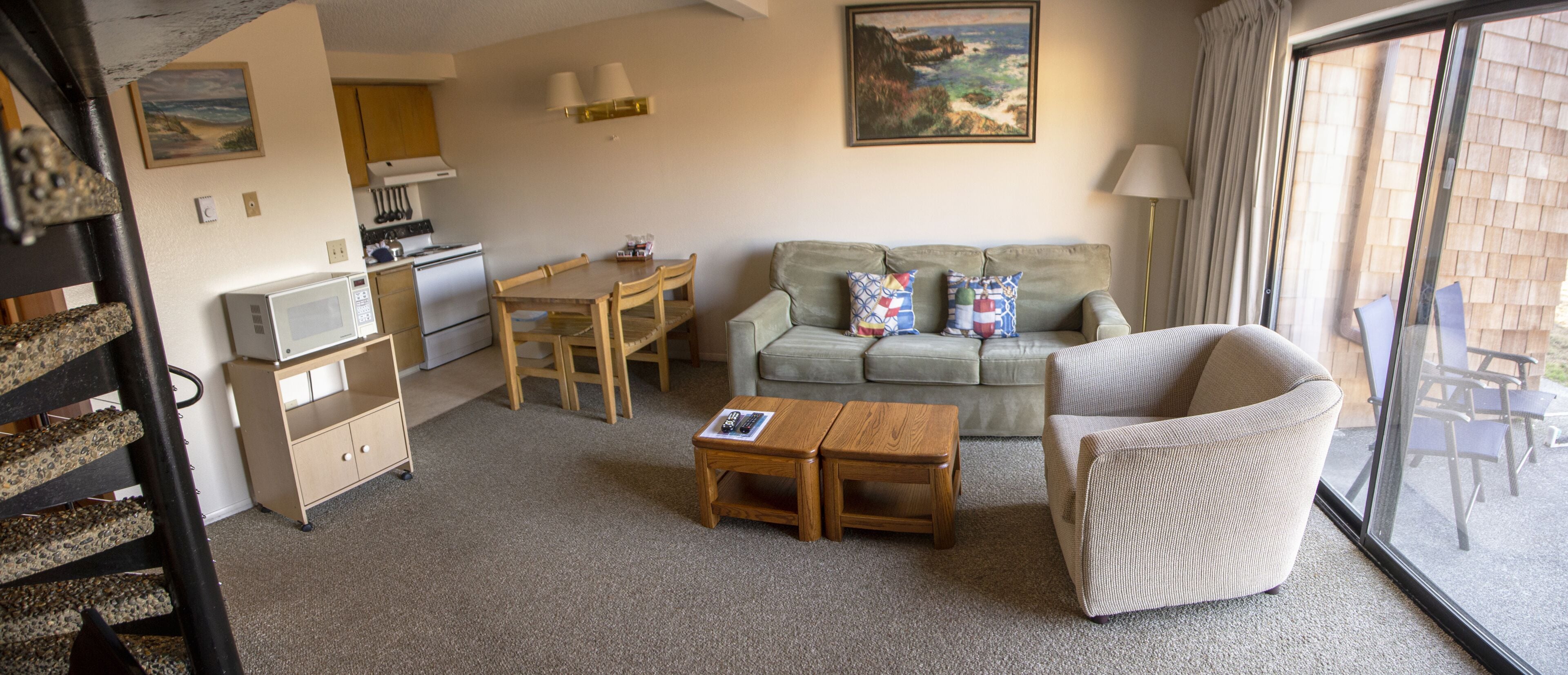 A cozy living room with a sofa, a coffee table, and a dining table. There is a kitchen area with a stove and microwave.