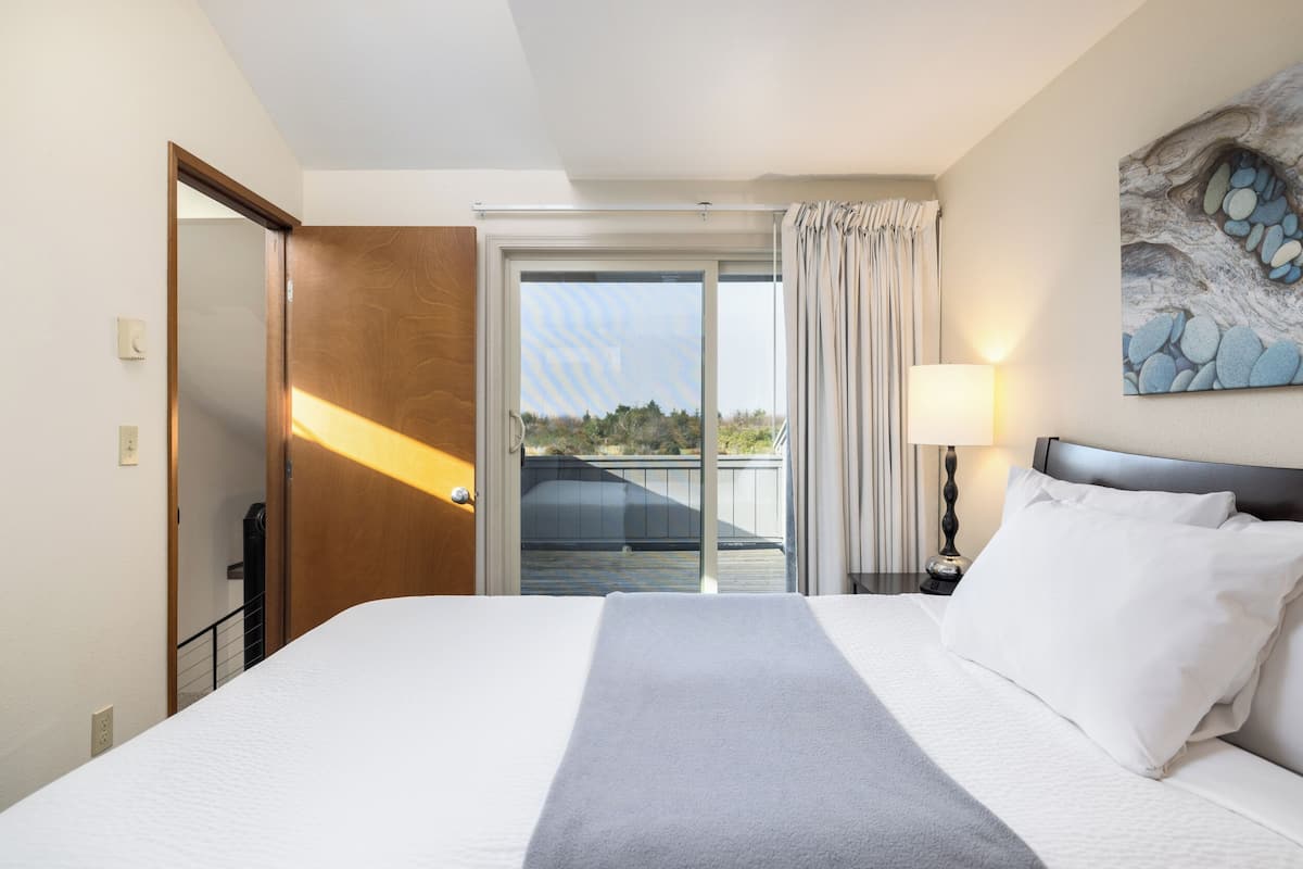 Habitación de hotel con una cama grande, un balcón con vistas, un cuadro en la pared y una lámpara en la mesita de noche.