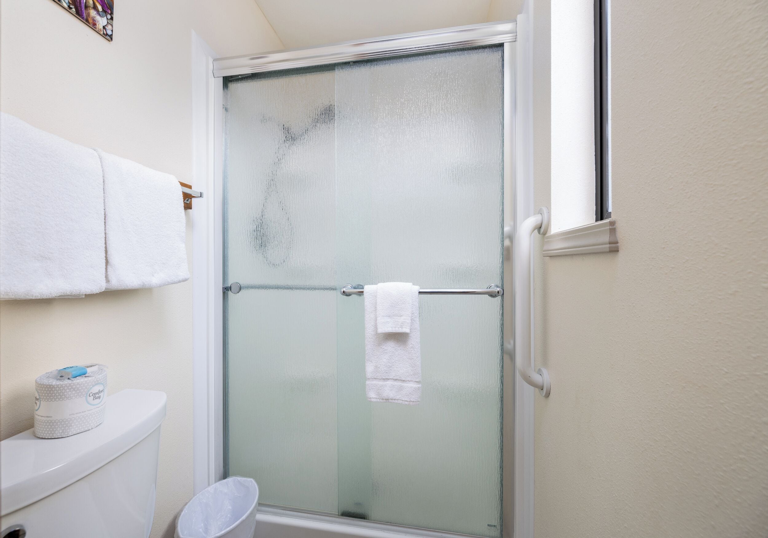 A bathroom with a glass-enclosed shower, a toilet, and a towel rack with two towels.