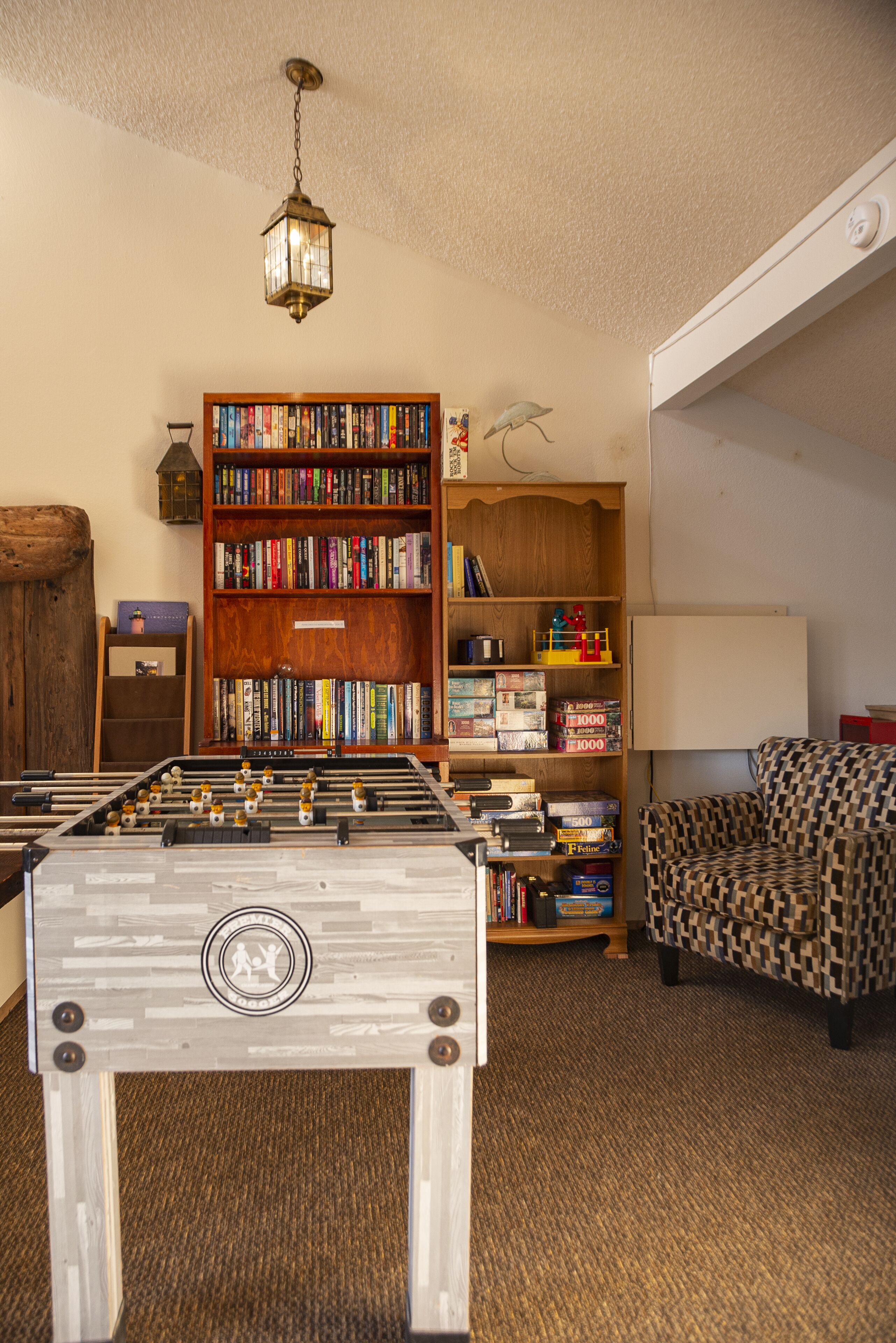A room with a foosball table, a bookshelf, and a patterned armchair.